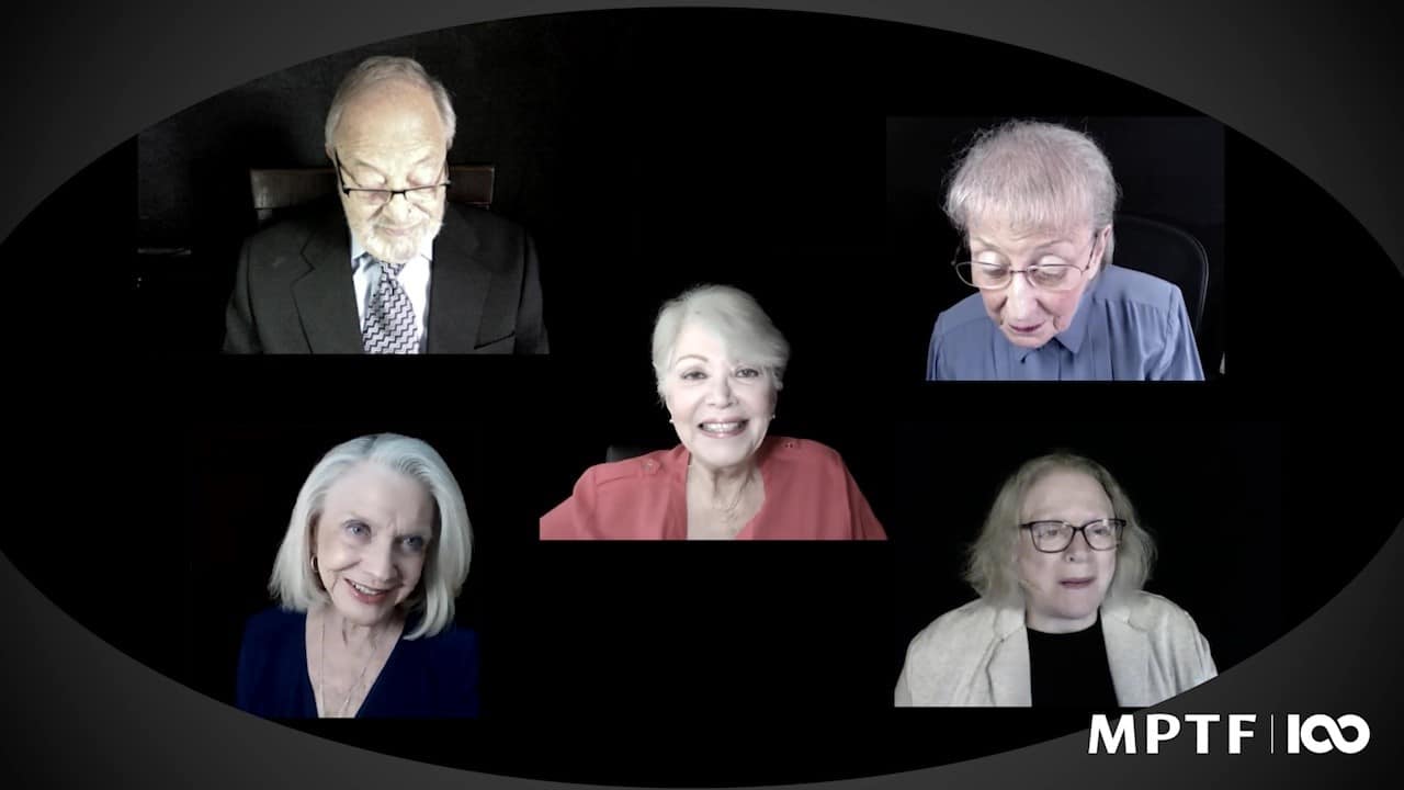 A group of older people are sitting in front of a black background.