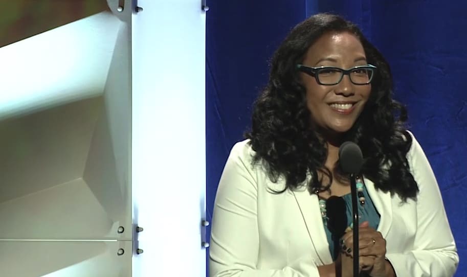 A woman in glasses is standing in front of a microphone.