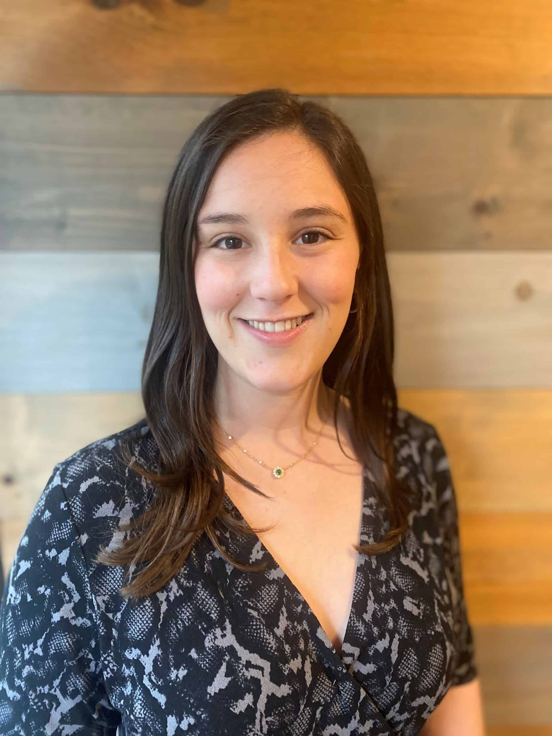 A woman smiling in front of a wooden wall.