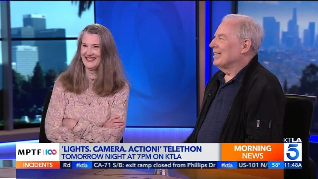 A man and woman are sitting on a television set.