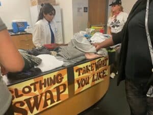 People participating in a clothing swap, taking and offering clothes at a designated table.